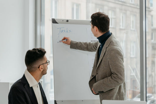 Deux hommes dans un bureau. Un homme écrit dans le tableau et l'autre personne regarde le tableau.
