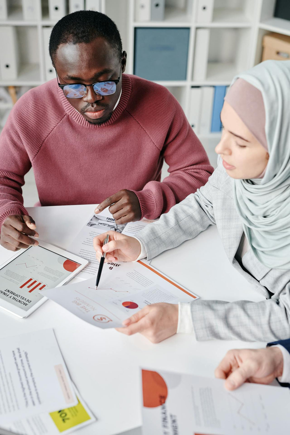 Homme et femme assis sur un bureau. La femme pointe un stylo sur un graphique présent dans un support papier. 