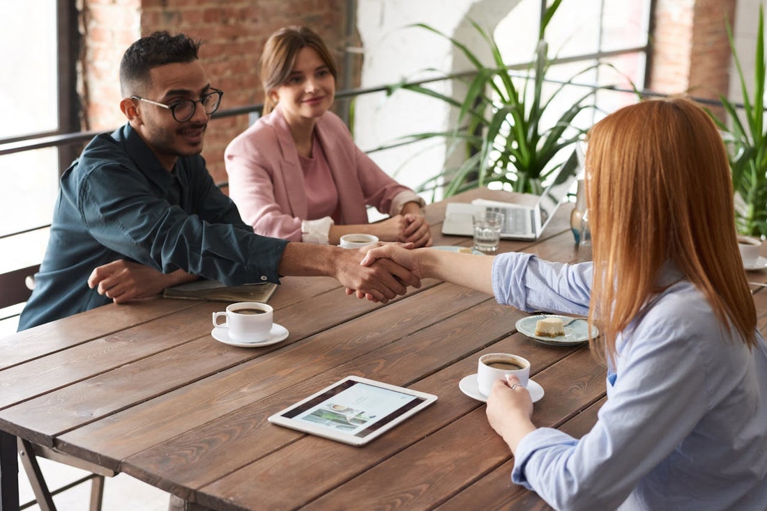 3 personnes assises sur une table dont deux se faisant une poignée de main. 