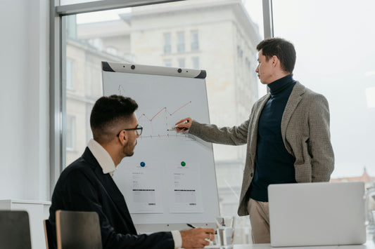 Deux hommes dans un bureau. Un homme pointe son marqueur dans le tableau comportant des données analytiques et l'autre personne regarde le tableau.