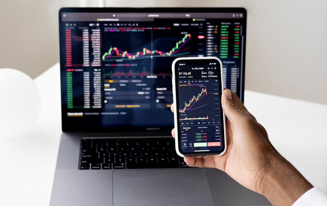 Ordinateur portable avec des données graphiques et main d’une personne tenant un téléphone portable contenant des analyses graphiques et chiffrées. 